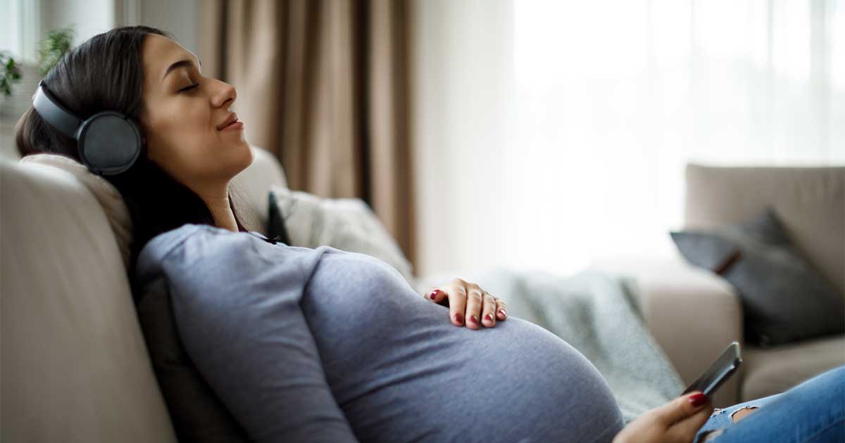 Bambo Nature Schwangerschaftskalender Woche 41 – eine Schwangere liegt auf dem Sofa und hört Musik
